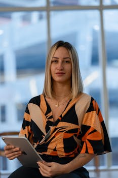 Confident businesswoman with tablet, sitting indoors with a blurred urban background.
