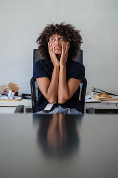 Contemplative woman in office, hands on face, expressing frustration.