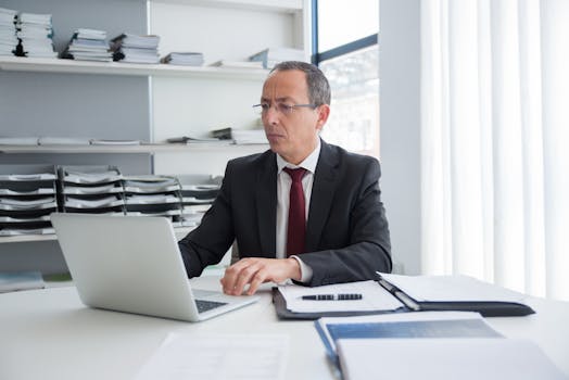 Focused businessman in a suit working at his office desk with a laptop and documents.
